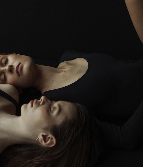 Woman practicing a gentle yoga pose in a minimalist dark room.